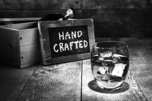 A sign that reads hand crafted with a glass of cocktail in front of it.