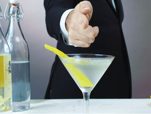 A craft cocktail in a martini with a suit-wearing mixologist behind it.