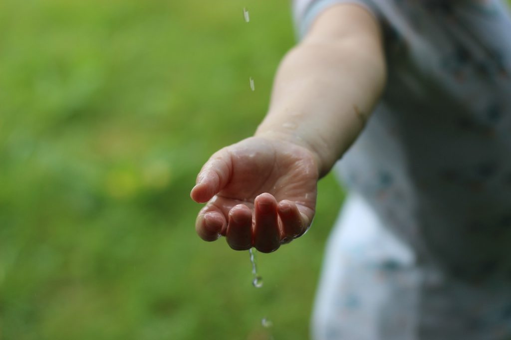 Hand stretching out to catch water drops outside.